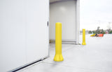 Two bright yellow bollards installed on a concrete loading dock area outside a white warehouse building, with a forklift visible in the background.